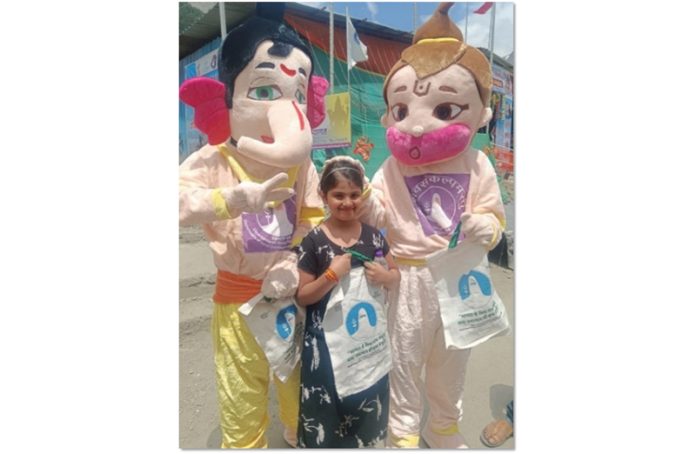 A girl posing with the mascots of Lord Ganesha and Lord Hanuman prepared from recycled waste.